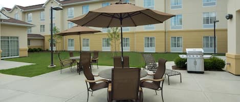 A patio area with outdoor seating, a grill, and a building in the background.