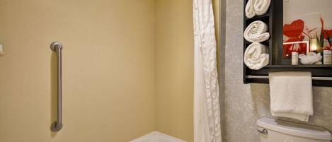 Ein Badezimmer mit Badewanne, Toilette, einer Handstange und einem Ablagefach mit Handtüchern.