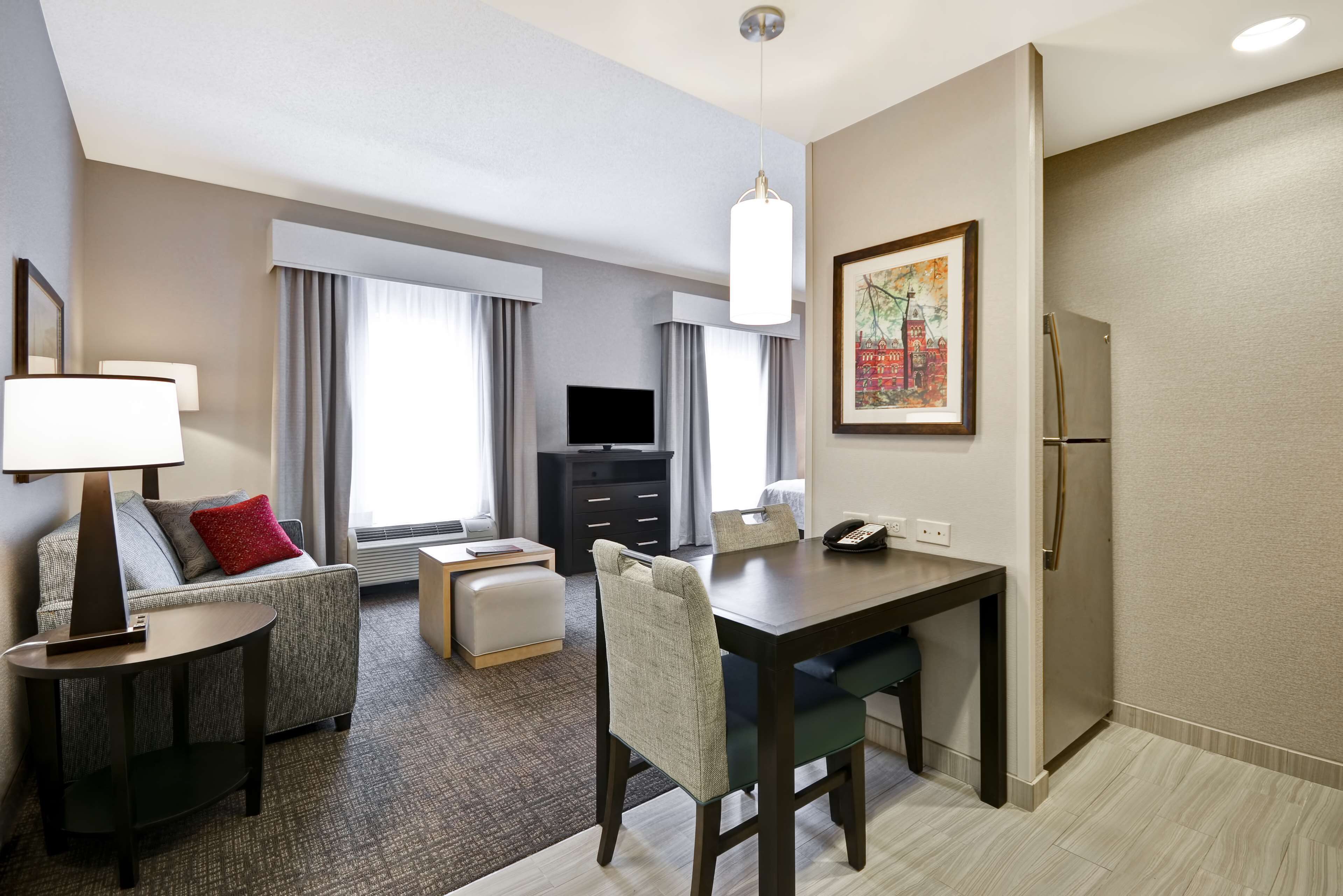 Habitación de hotel con zona de comedor, sofá, televisor y refrigerador.