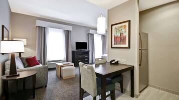 Habitación de hotel con zona de comedor, sofá, televisor y refrigerador.