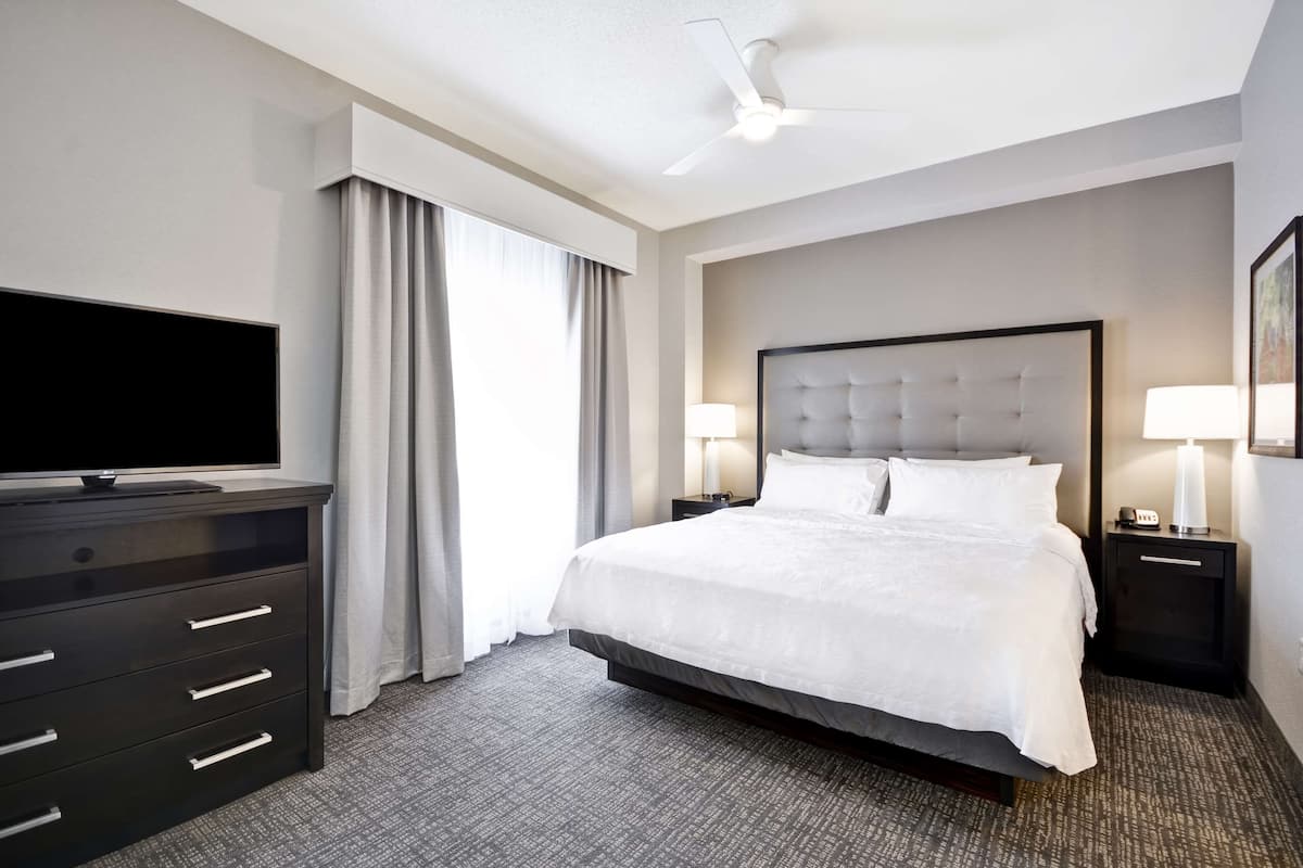 Quarto de hotel com uma cama grande, televisão de tela plana, cômoda e ventilador de teto.