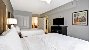 A hotel room with two beds, a television, a painting on the wall, and a ceiling fan.