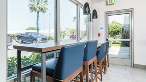 A modern interior with a long table and blue chairs, large windows with a view of palm trees and parked vehicles outside. - Holiday Inn Express Hotel & Suites San Diego Otay Mesa by IHG (San Diego)