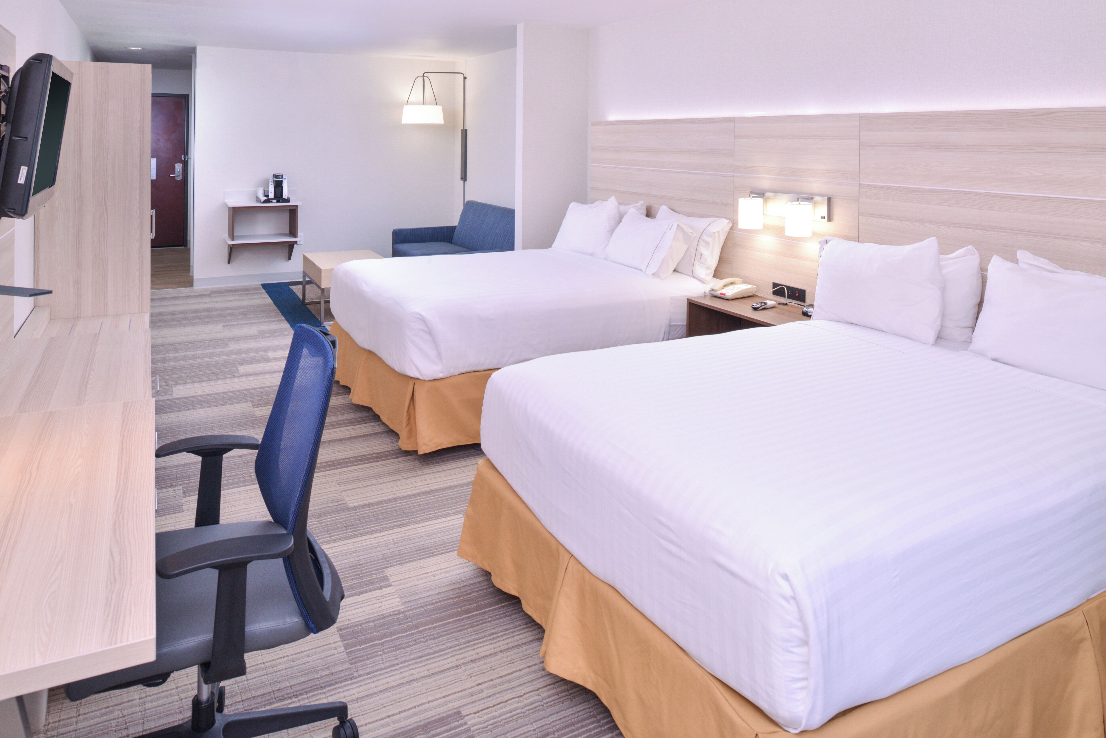 A hotel room with two beds, a desk, a chair, and a small table.