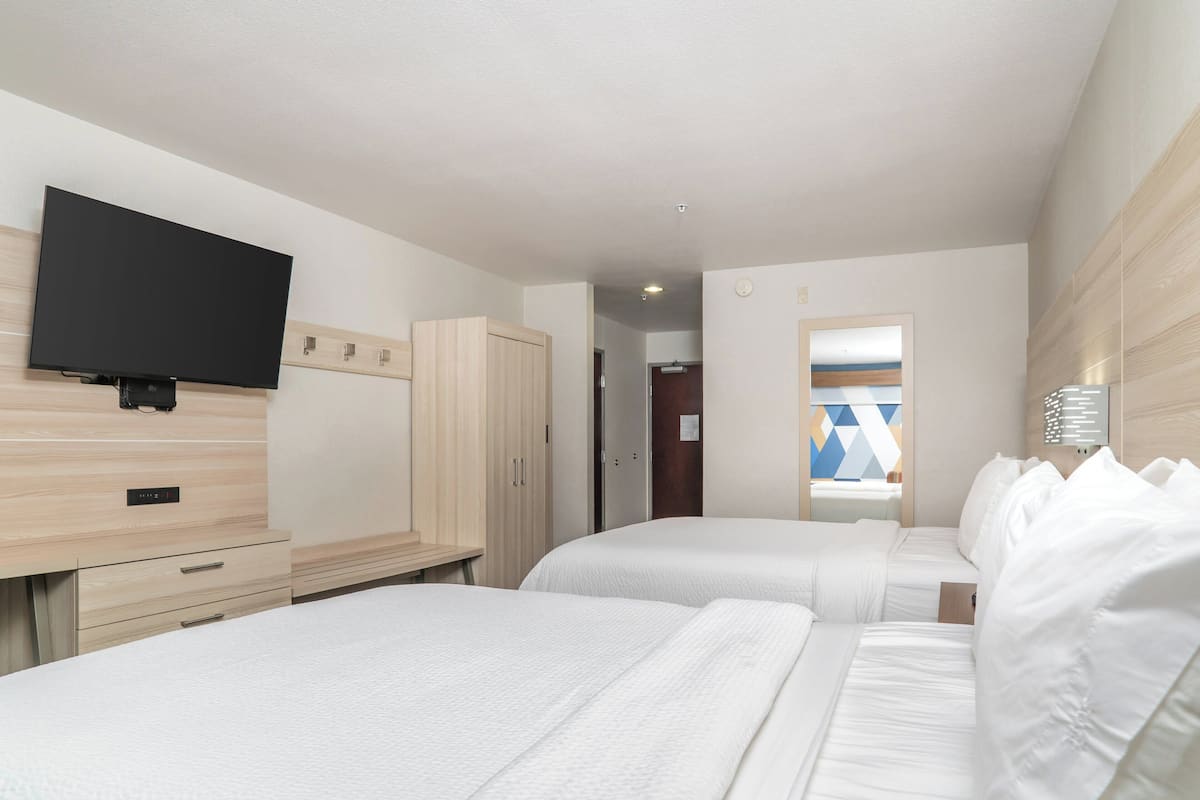 Une chambre d’hôtel avec deux lits, un téléviseur fixé au mur et une armoire en bois.