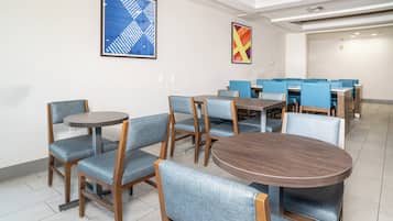 Un espace de restauration d'hôtel avec des tables rondes et des chaises rembourrées de tissu bleu.