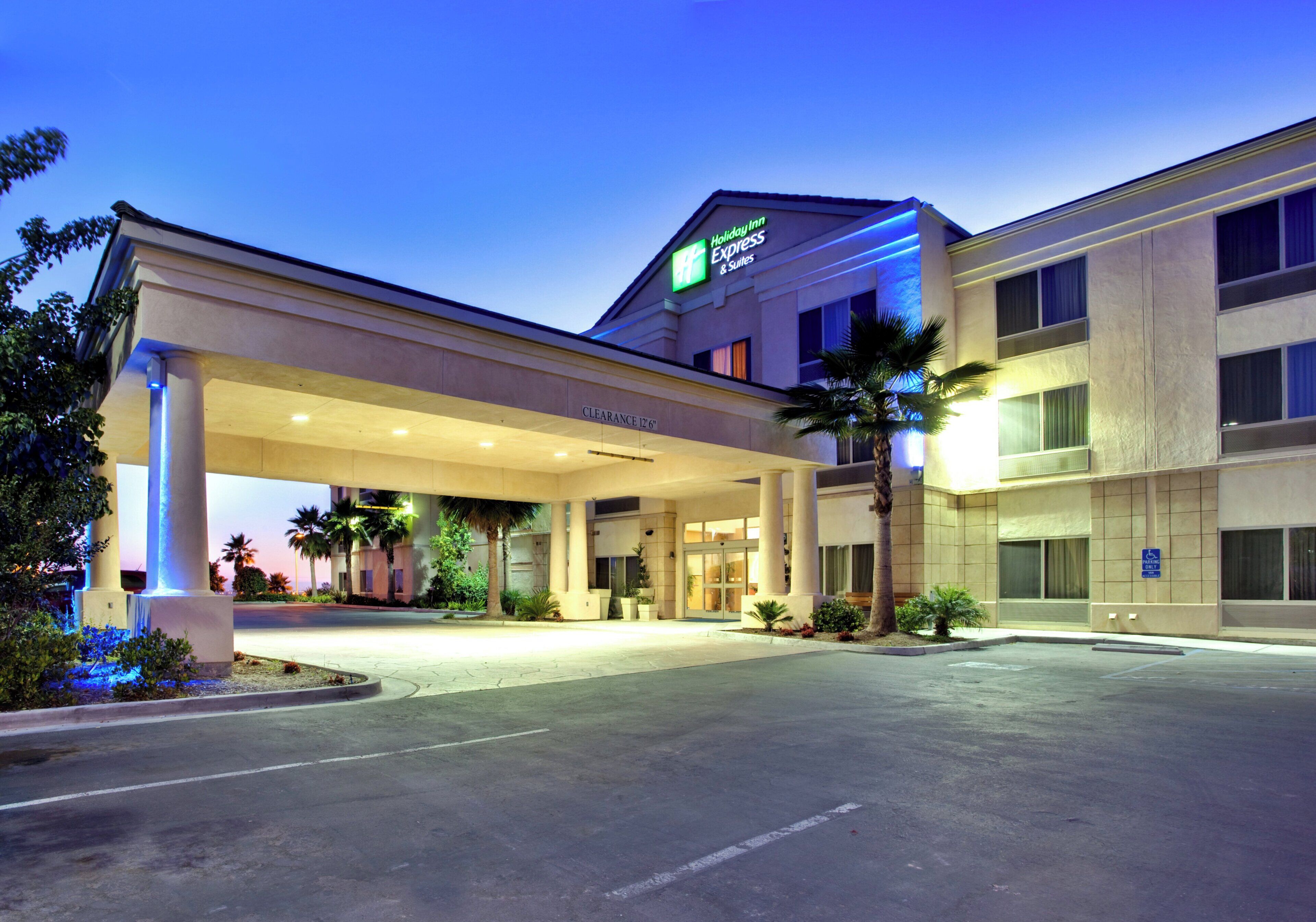 A Holiday Inn Express & Suites building with a covered entrance, palm trees, and a clear sky.