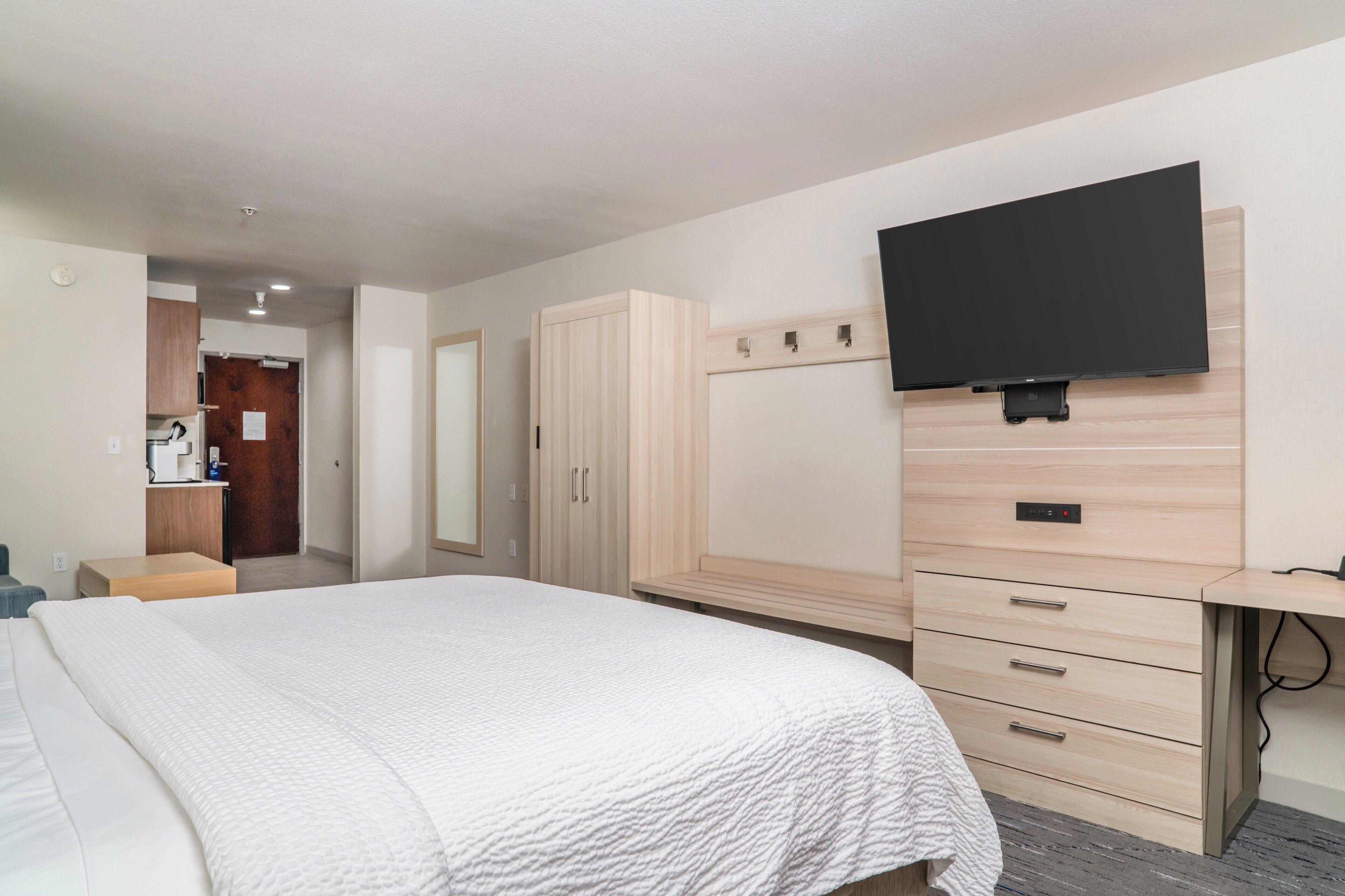 A bedroom with a large bed, a TV mounted on the wall, and a wooden wardrobe.