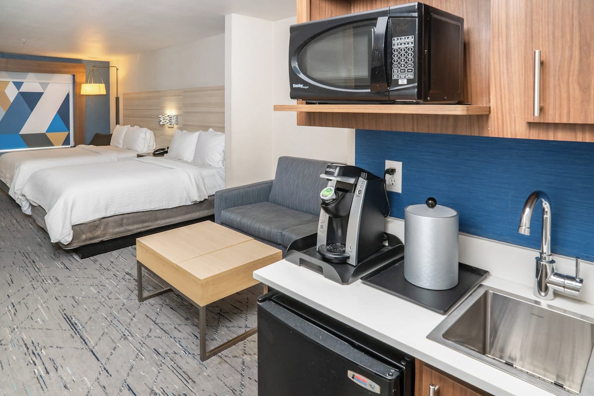 Une chambre d’hôtel compacte comprenant un lit, un canapé, une machine à café, un four à micro-ondes et un évier.