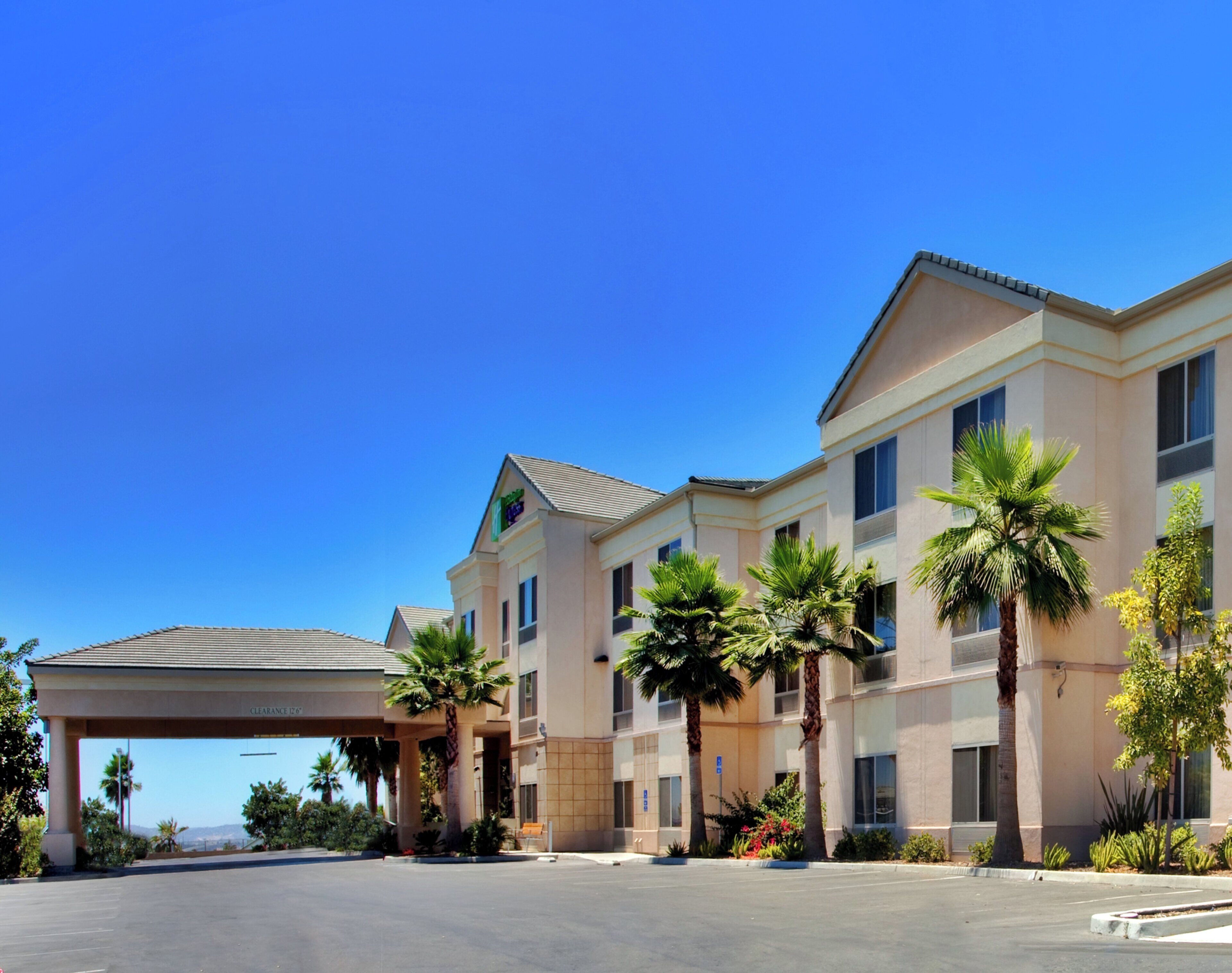 A hotel with a covered parking area, multiple floors, and palm trees.