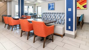 A modern dining area with orange chairs, a wooden table, and a patterned wall. - Holiday Inn Express Hotel & Suites San Diego Otay Mesa by IHG (San Diego)