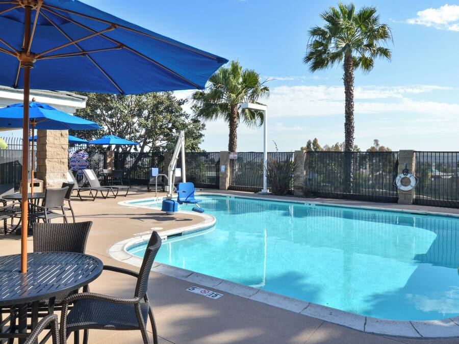A swimming pool with a surrounding deck, lounge chairs, and umbrellas.