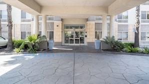 A building entrance with a covered walkway, glass doors, and palm trees. - Holiday Inn Express Hotel & Suites San Diego Otay Mesa by IHG (San Diego)