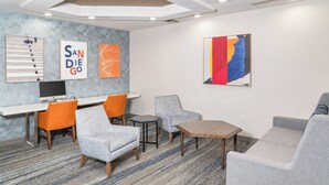 A modern lounge area with a flat-screen TV, orange and gray chairs, a gray sofa, and a wooden coffee table. - Holiday Inn Express Hotel & Suites San Diego Otay Mesa by IHG (San Diego)