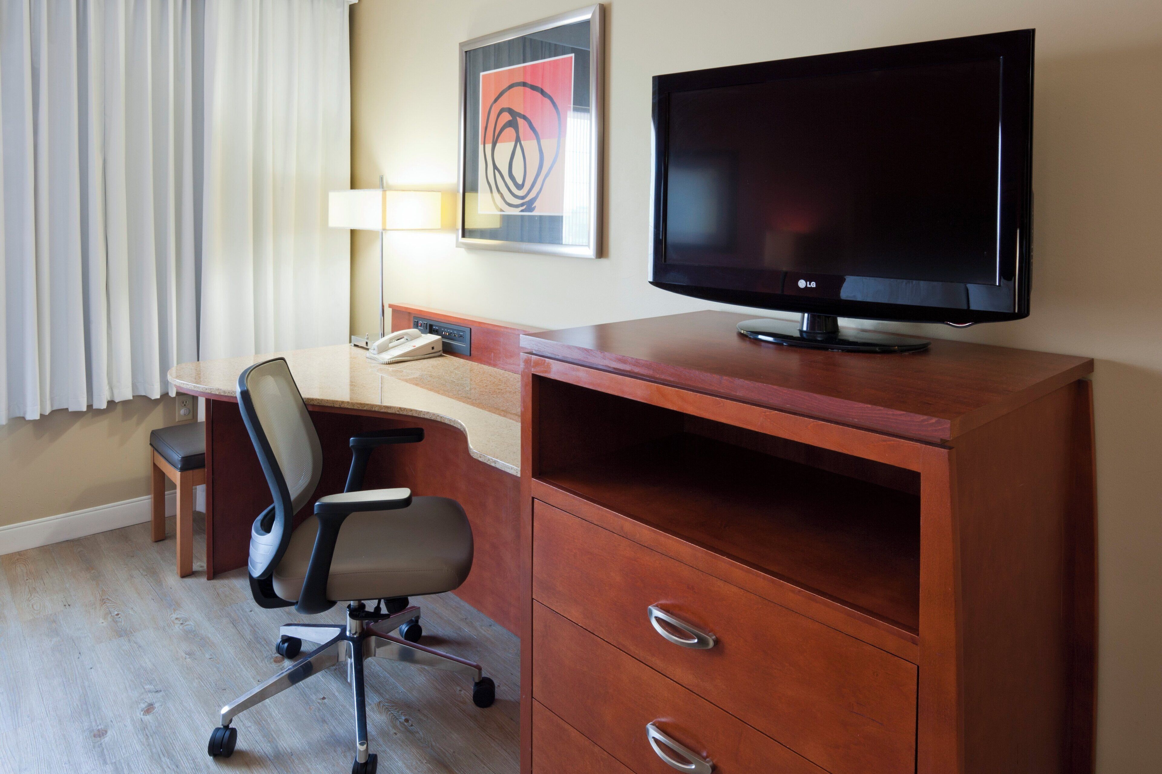 A hotel room with a desk, chair, television, and a telephone.