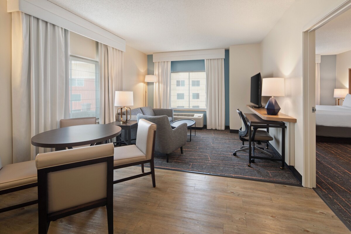 Une chambre d’hôtel comprenant un lit, un bureau, une chaise, un canapé, une télévision et une fenêtre avec des rideaux.