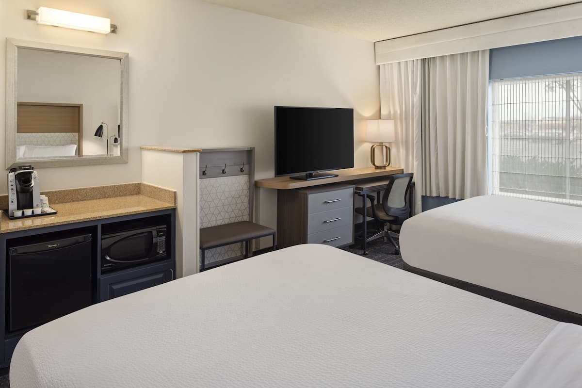 Habitación de hotel con cama, escritorio con televisor, microondas, cafetera y ventana con cortinas.