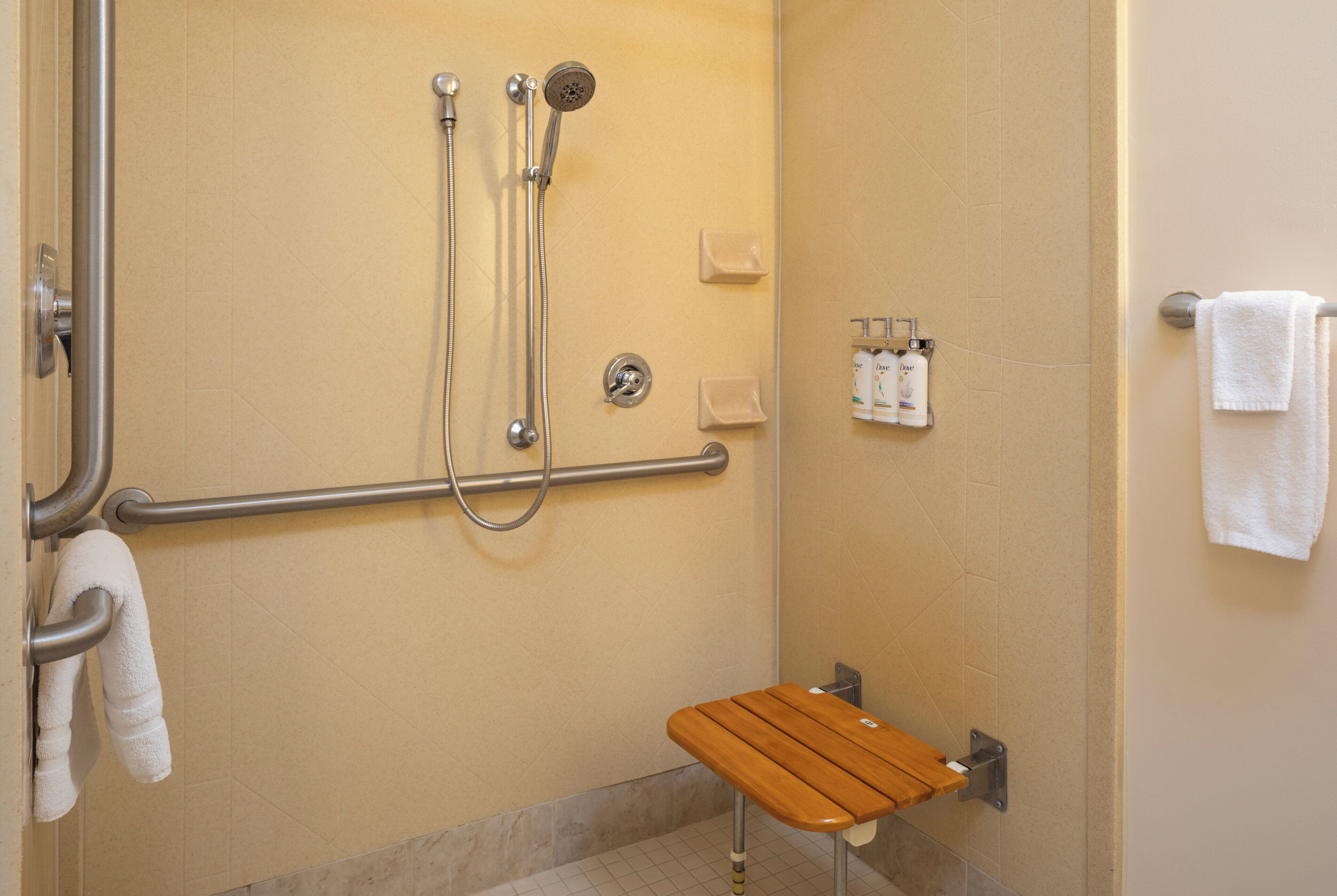 A shower area with a grab bar, a wooden bench, and hand soap dispensers.