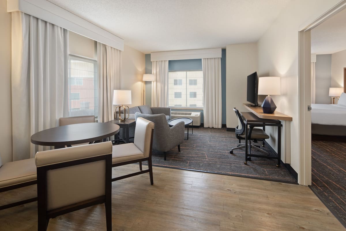 Habitación de hotel con cama, escritorio, silla, sofá, televisión y ventana con cortinas.