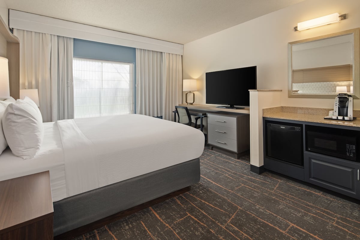 Habitación de hotel con una cama grande, un escritorio con televisor, cafetera y microondas.