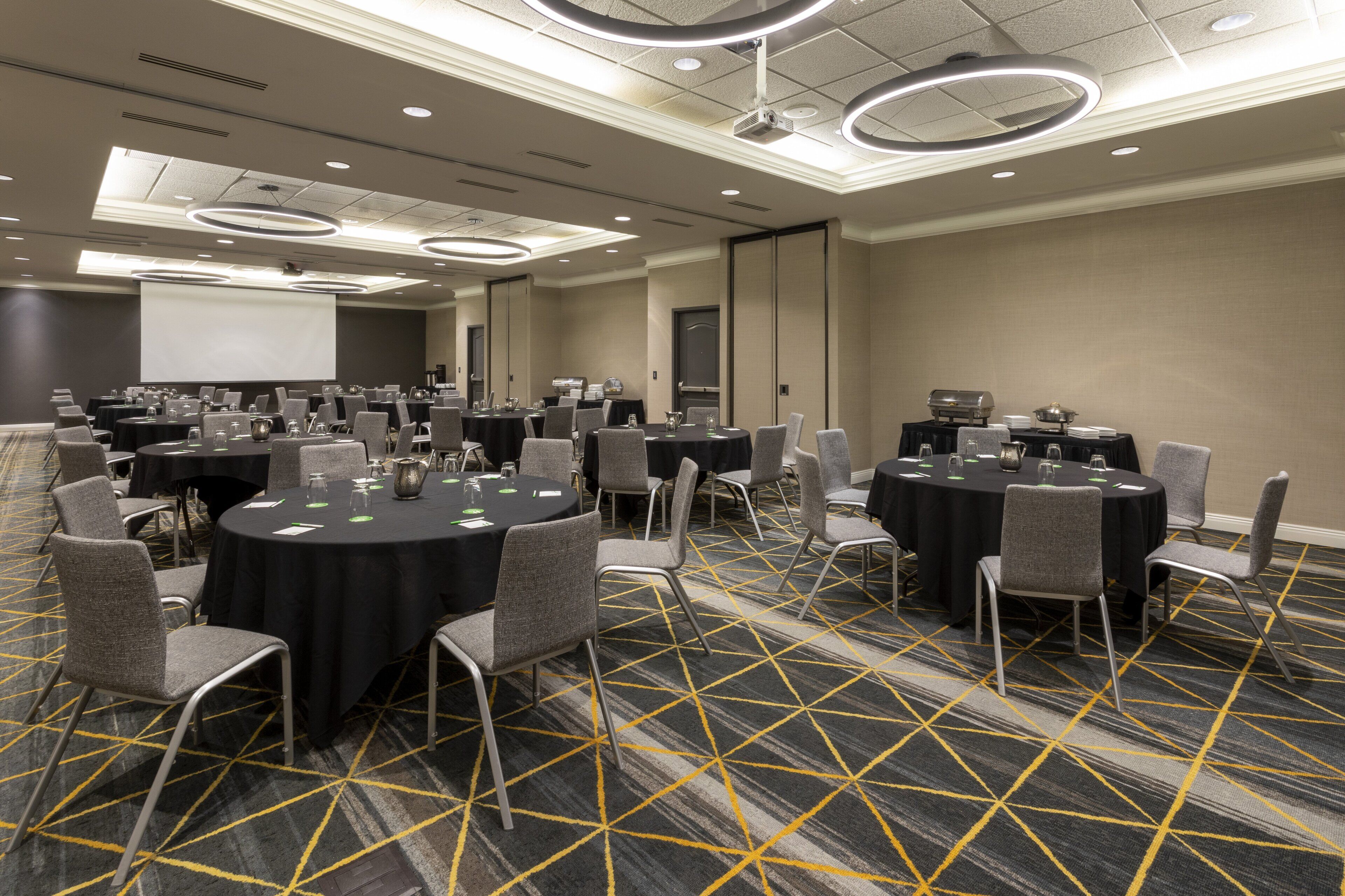 A conference room with multiple round tables, chairs, and a large screen.