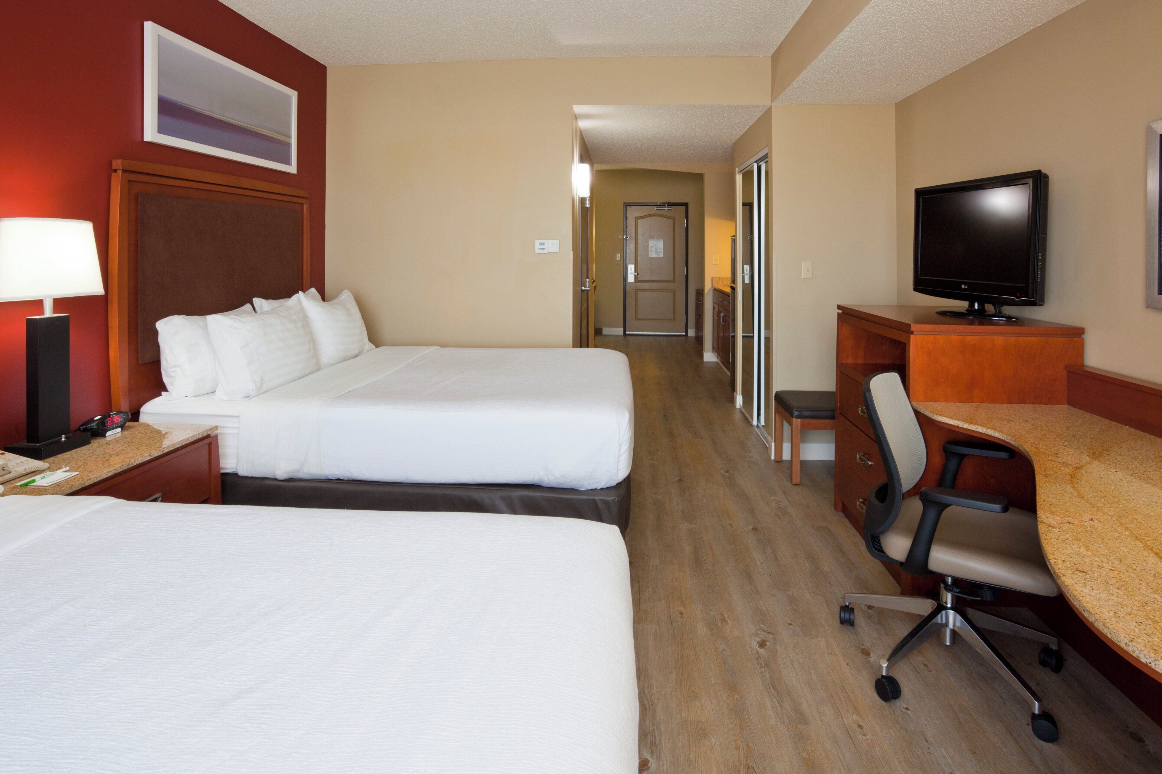 Habitación de hotel con dos camas, un escritorio, una silla, un televisor y una lámpara.
