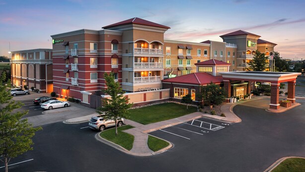 A multi-story hotel with a red and beige facade, multiple balconies, and a parking lot. - Holiday Inn Hotel & Suites Maple Grove Nw Mpls-Arbor Lks by IHG (Maple Grove)
