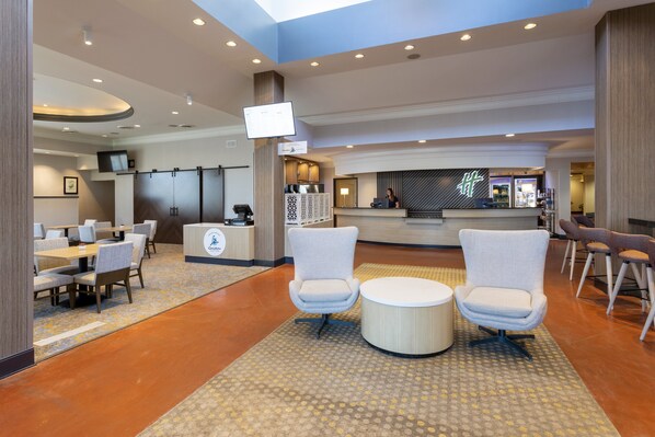 Un hall d’hôtel moderne doté d’un comptoir d’accueil, d’un espace salon et d’un grand écran.