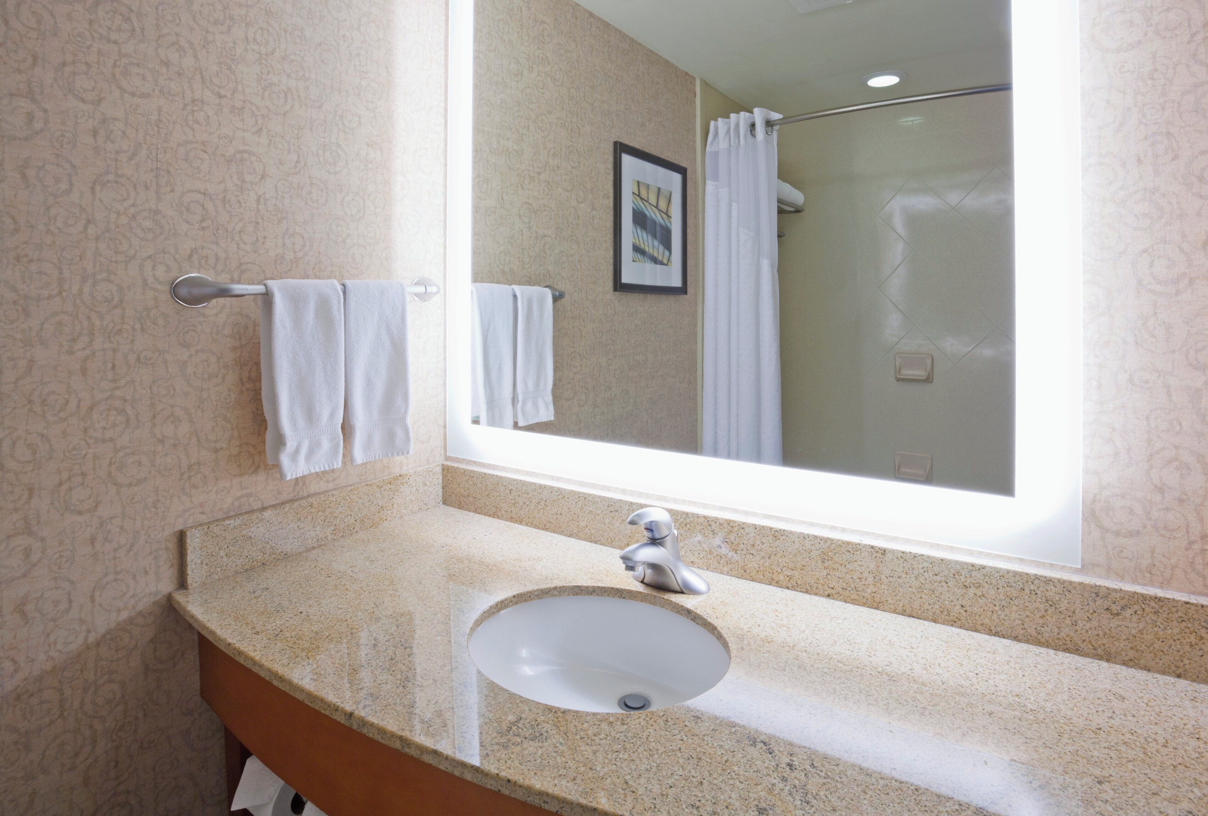 A bathroom with a granite countertop, a sink, a mirror, and a shower visible in the reflection.