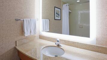 A bathroom with a granite countertop, a sink, a mirror, and a shower visible in the reflection.