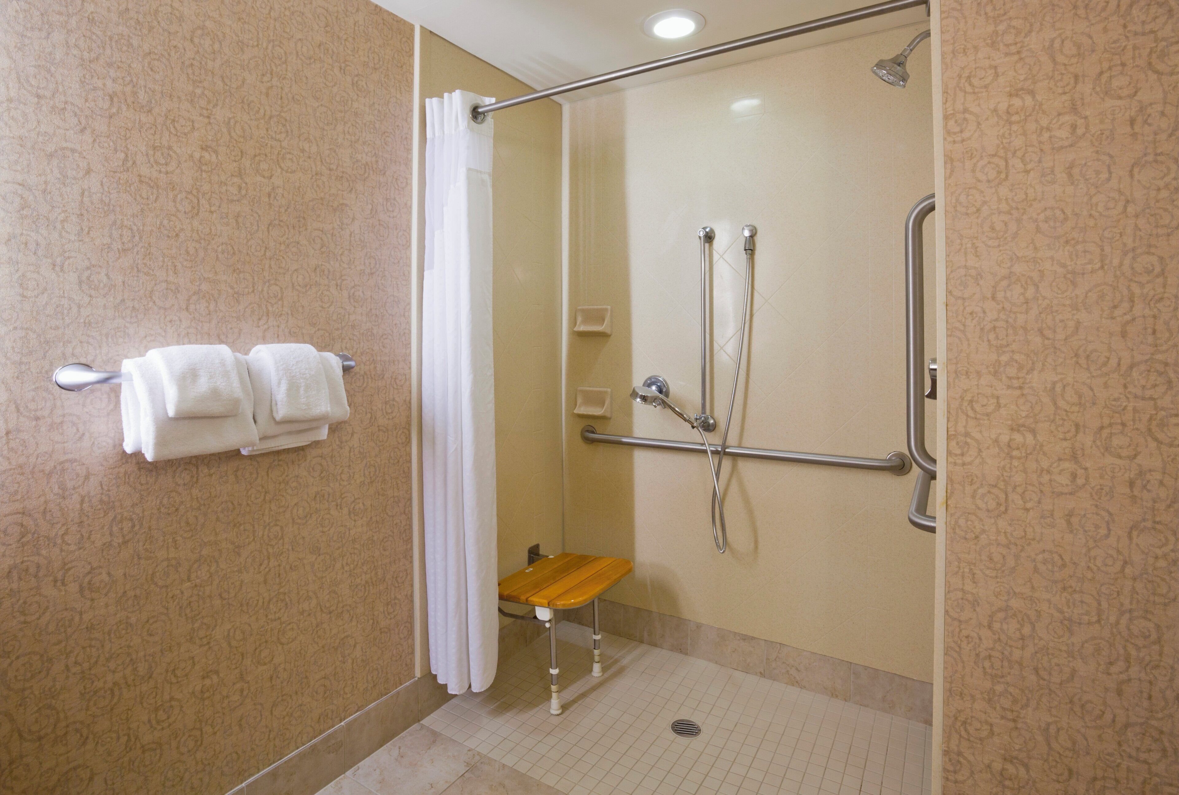 A shower area with a glass door, a grab bar, and a bench.