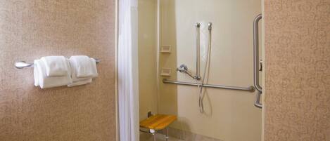 A shower area with a glass door, a grab bar, and a bench.