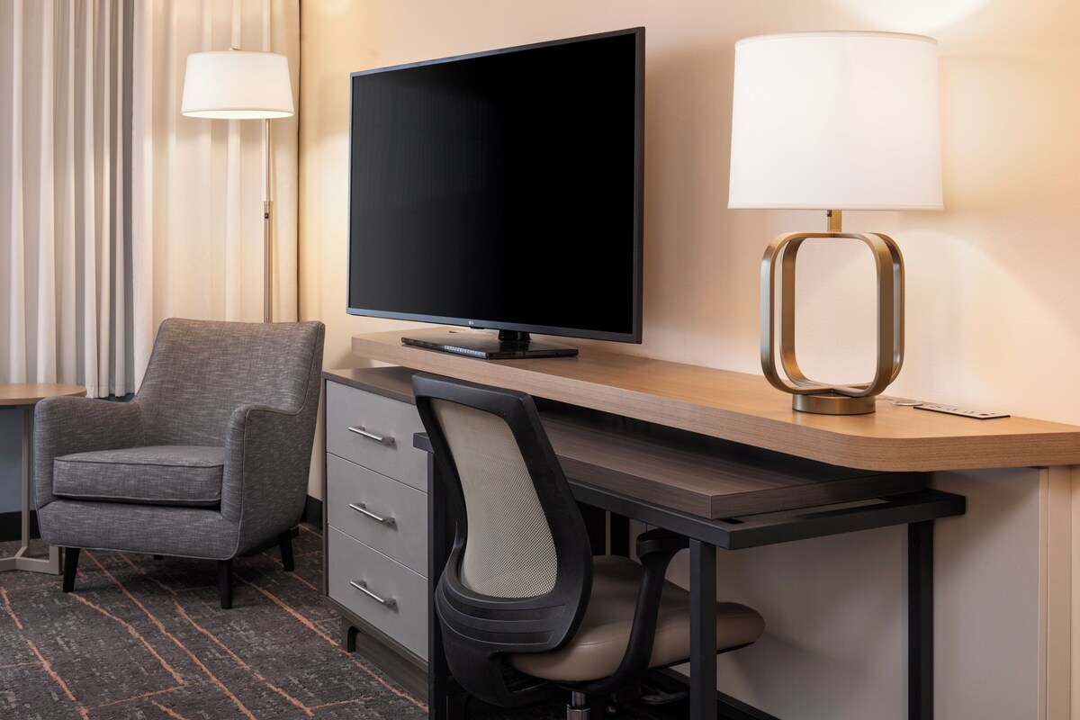 Une chambre d’hôtel équipée d’une télévision à écran plat, d’un bureau avec une lampe, d’une chaise et d’une commode.