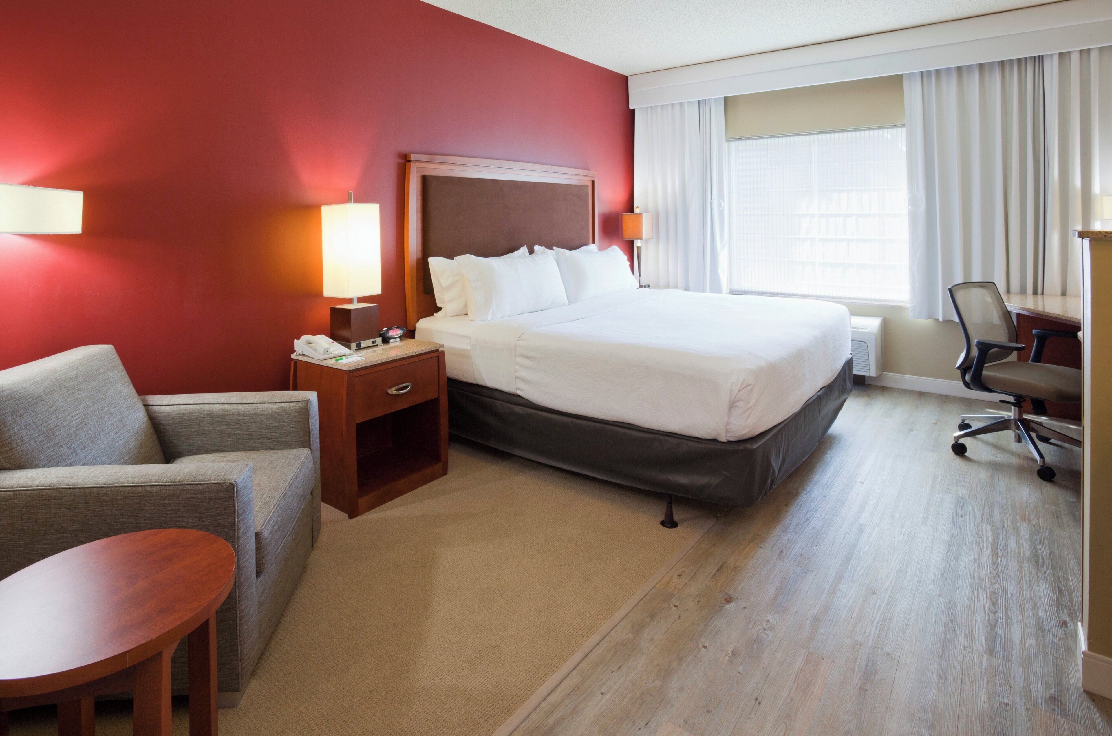 A hotel room with a bed, a desk, a chair, a sofa, and a window with curtains.