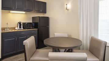 Cocina compacta con armarios oscuros, un refrigerador negro, un microondas y una cafetera. Hay una mesa redonda con dos sillas color beige.