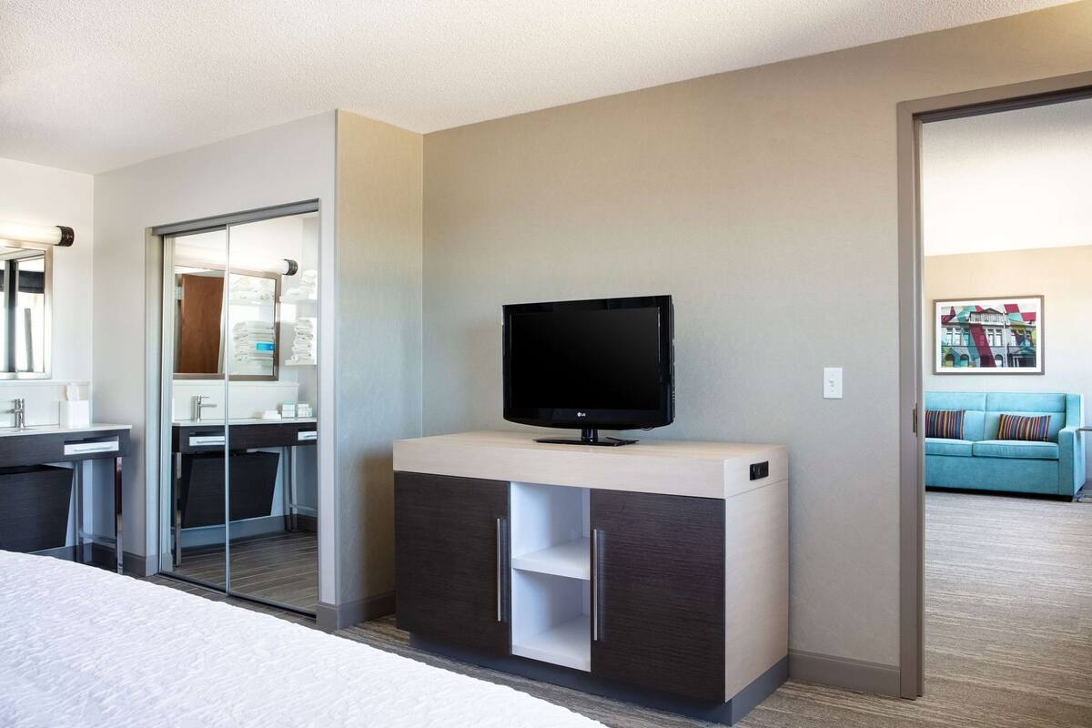A hotel room with a TV on a cabinet, a mirror, a bathroom with a towel rack, and a blue sofa in the background.