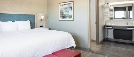 A hotel room with a bed, a bench, a bathroom, and a wall-mounted picture.