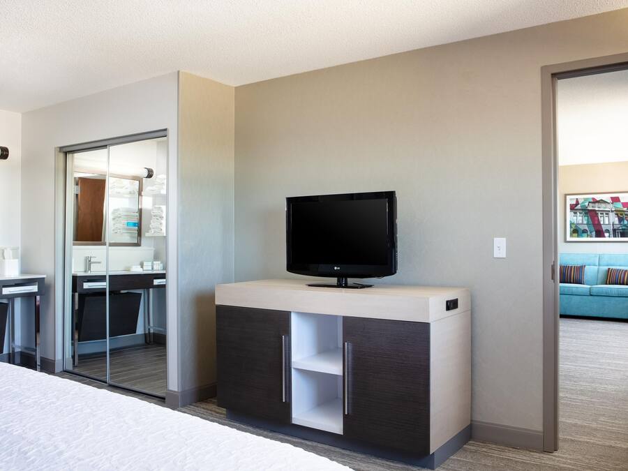 A hotel room with a bed, a TV on a stand, a bathroom with a mirror, and a sofa in the corner.