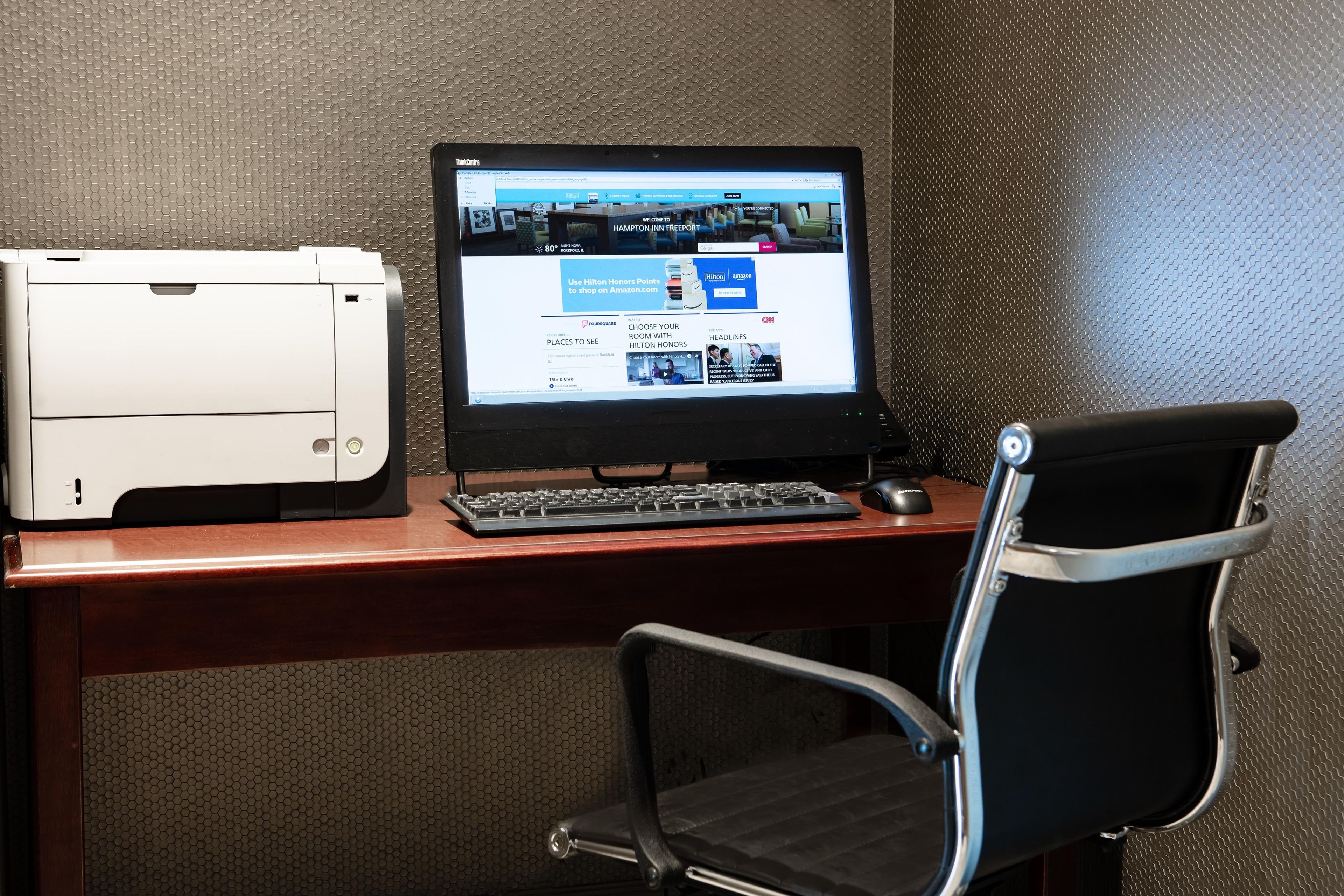A desk with a laptop, a printer, and a chair.