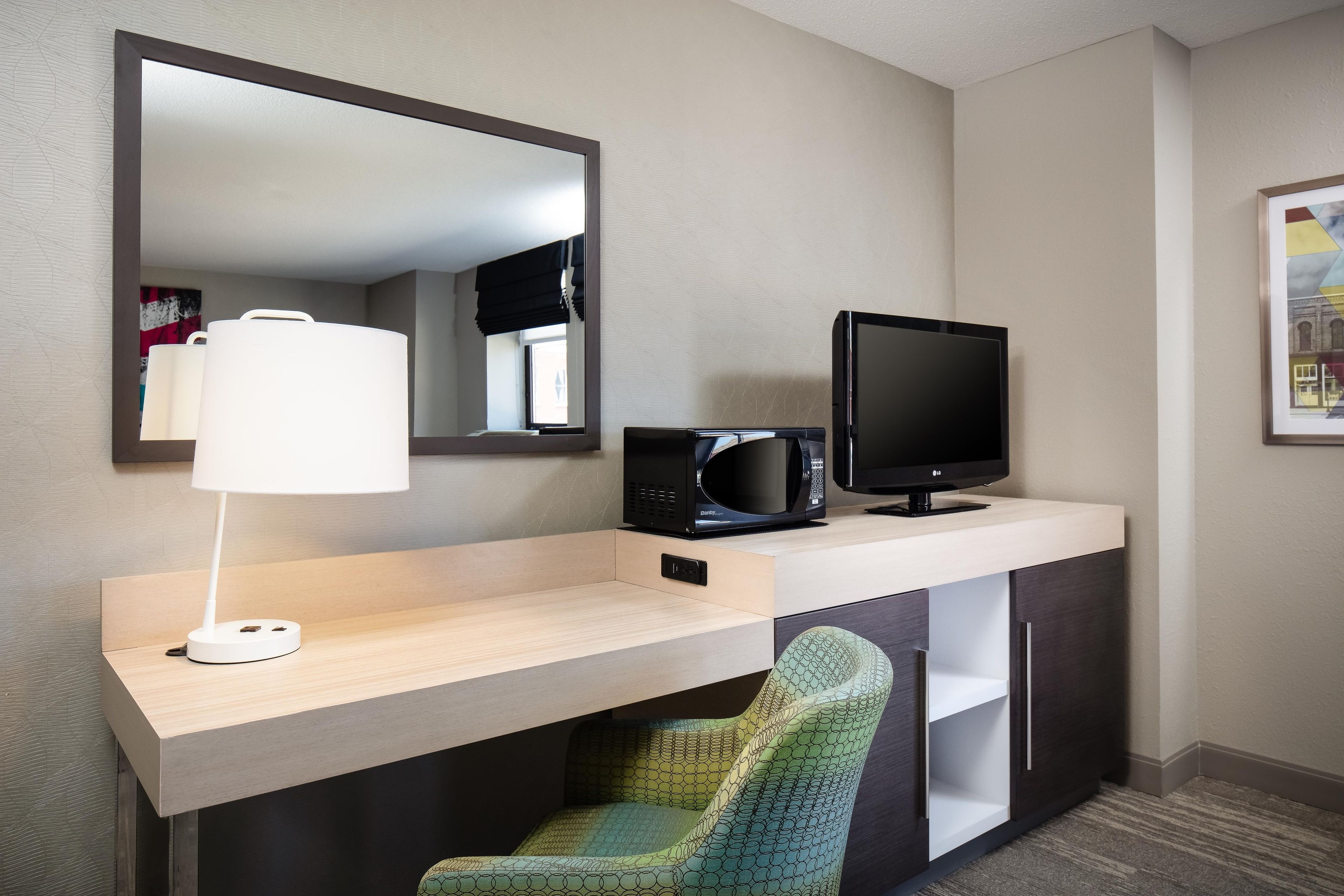 Et hotelværelse med skrivebord, fladskærm, lampe, mikroovn og stol.