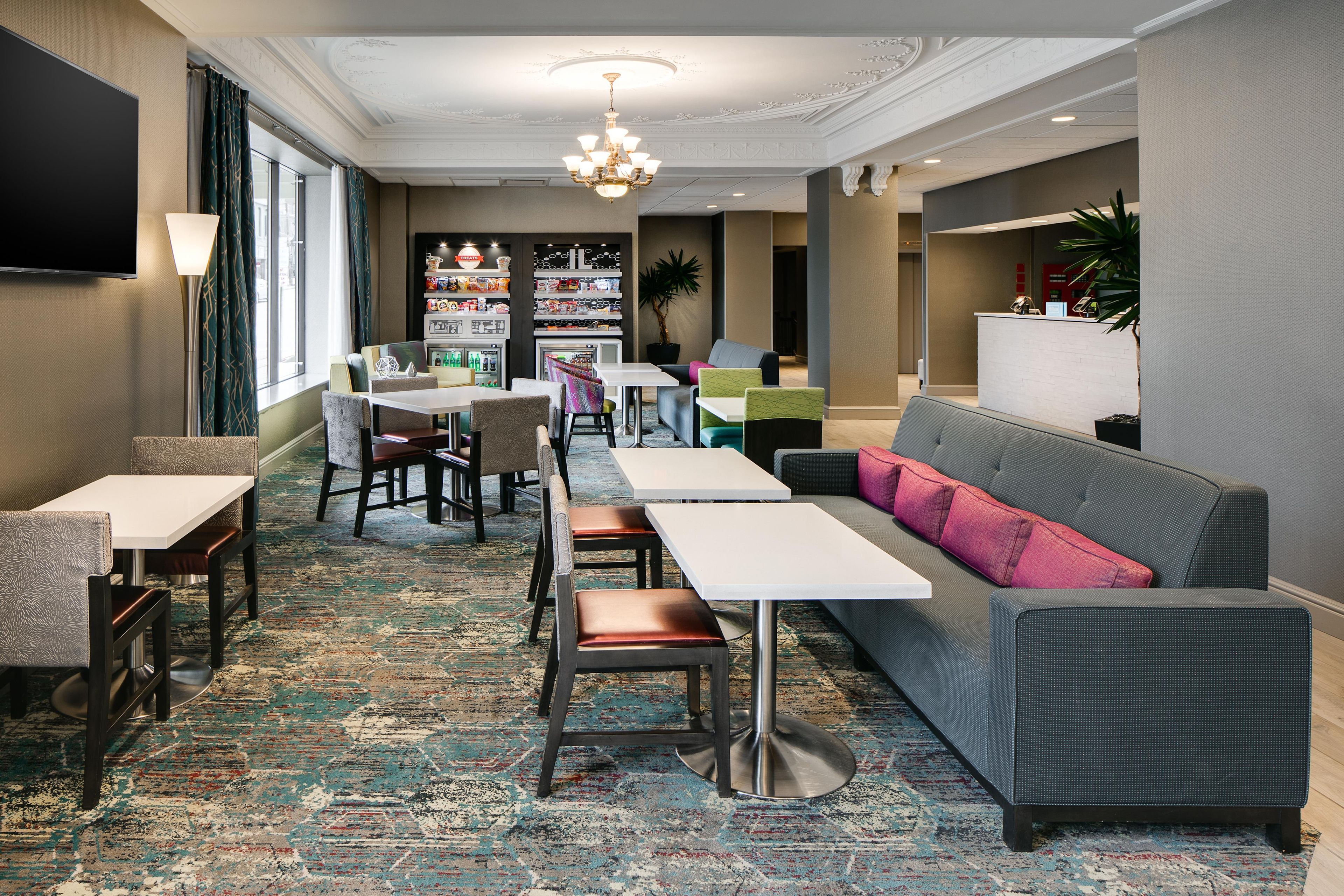Un vestíbulo de hotel con zona de bar, arreglos de asientos y una pantalla de televisión.