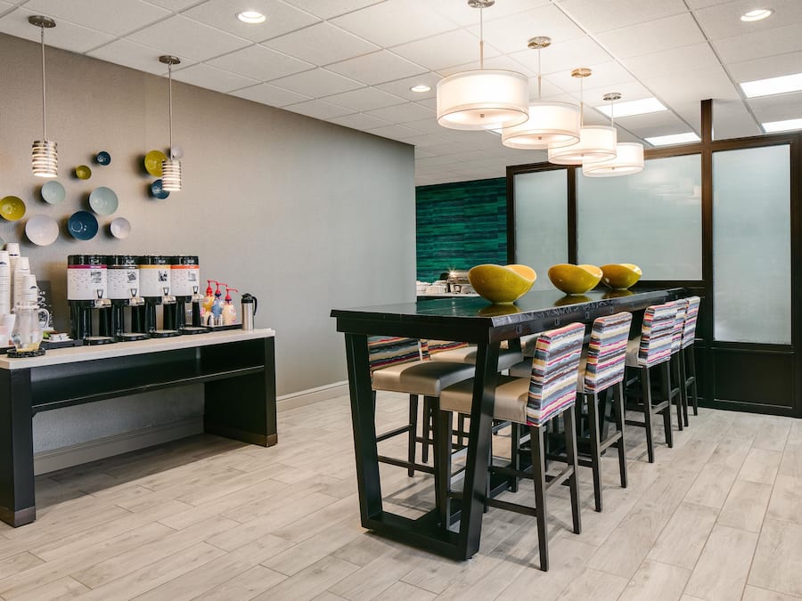 A modern bar area with a long counter, multiple beverage dispensers, and a seating arrangement with colorful chairs.