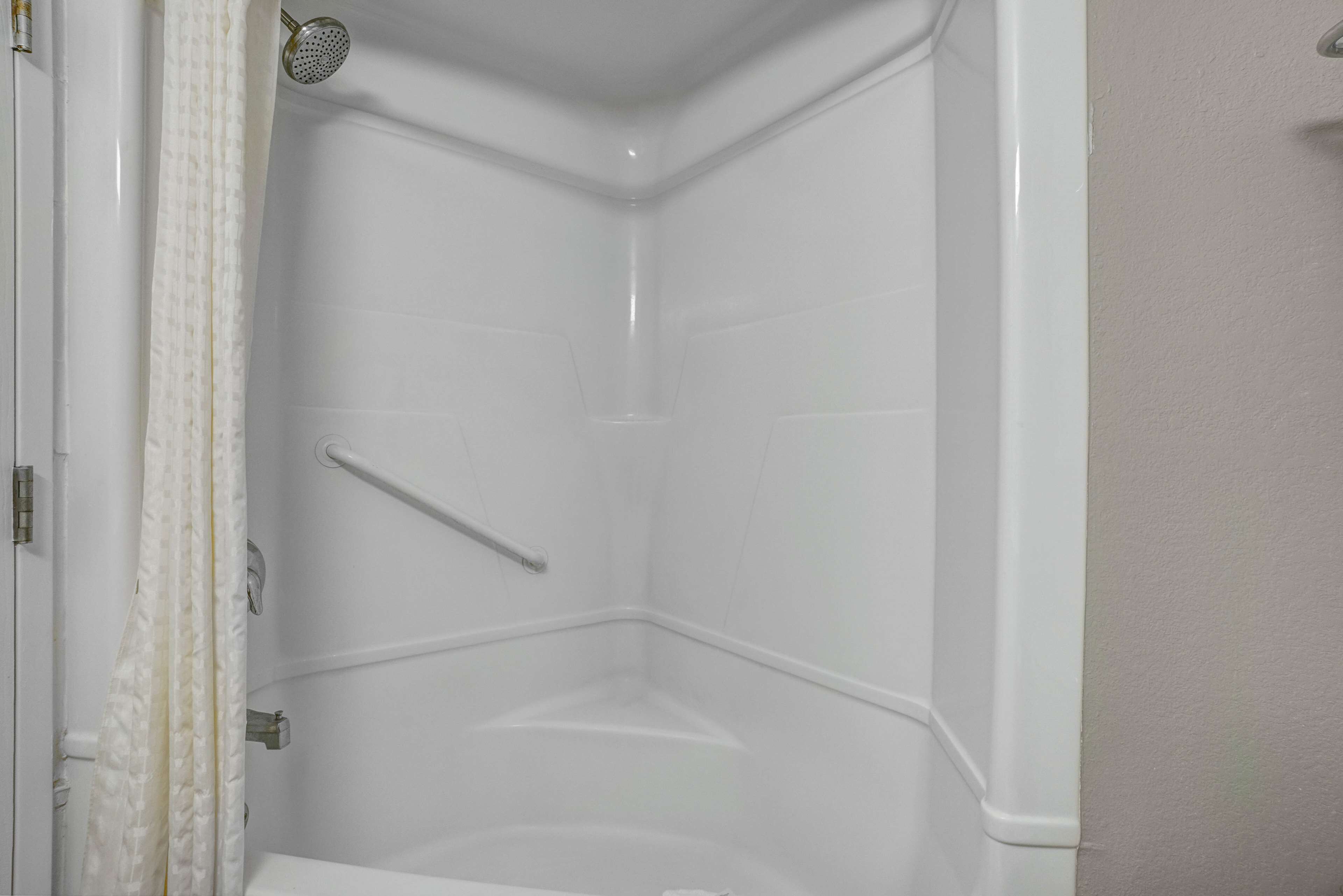 A corner shower with white tiles, a handheld showerhead, and a grab bar.