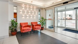 Un área de recepción con dos sillas rojas, una lámpara fijada a la pared y una puerta de vidrio que da al exterior.