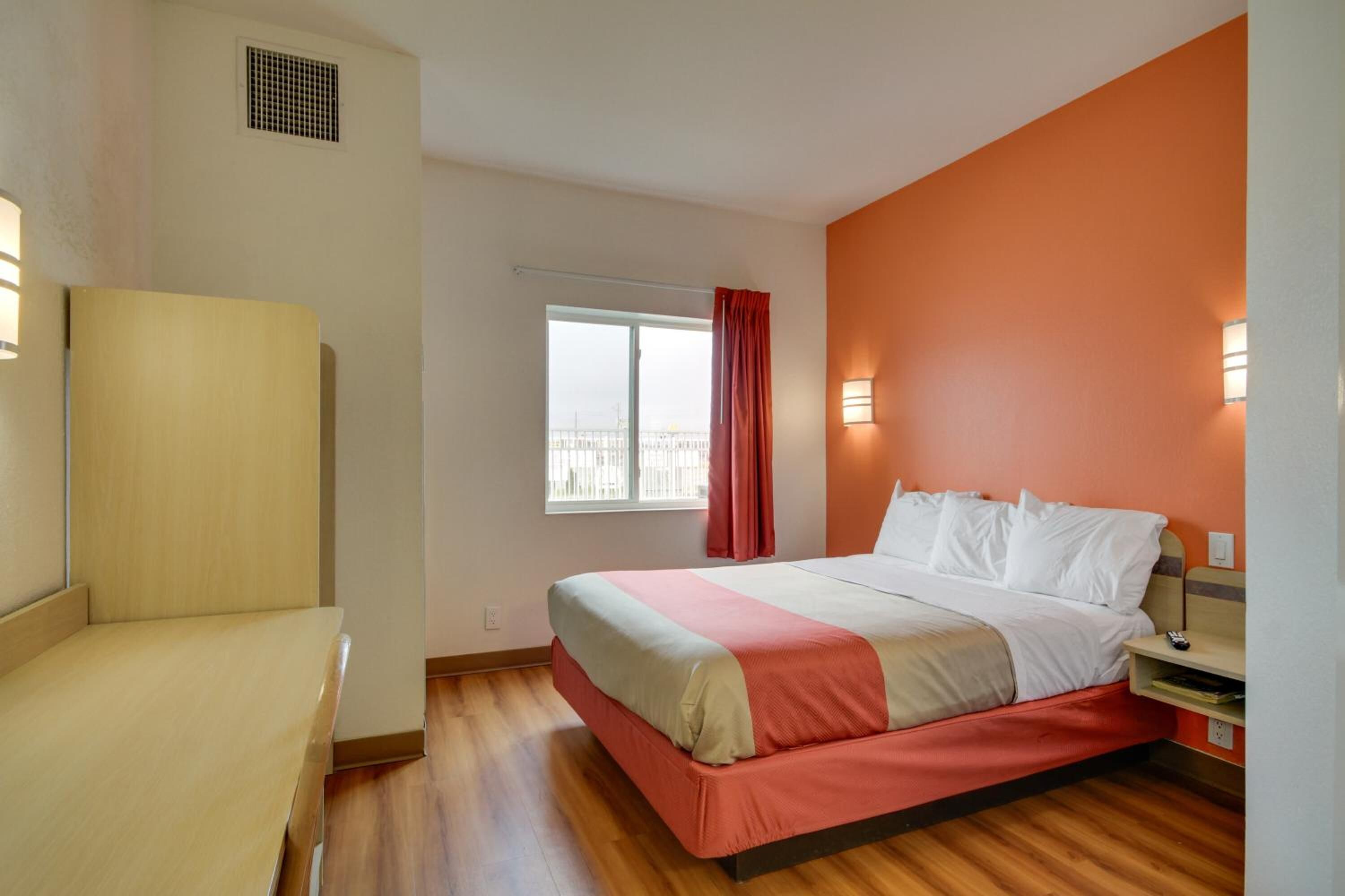 Habitación de hotel con cama, una silla, ventana con cortinas y una lámpara en la pared.