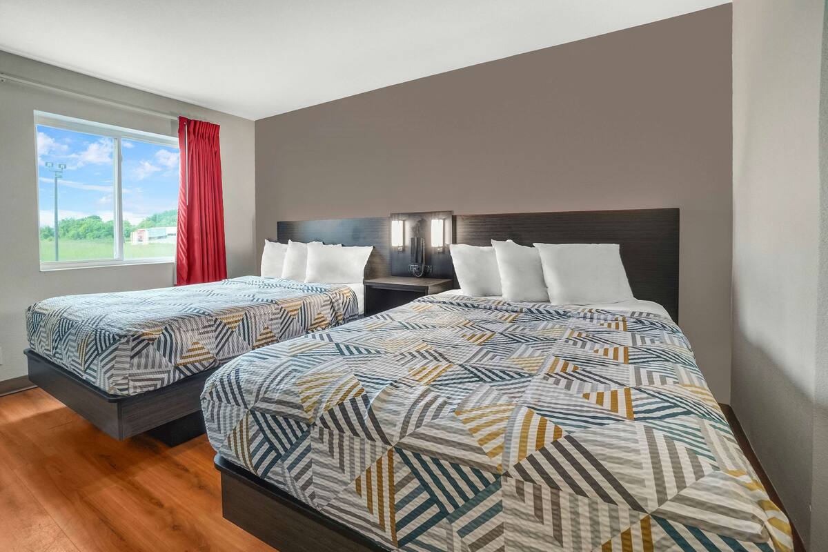 A hotel room with two beds, a large window with a view, and a red curtain.