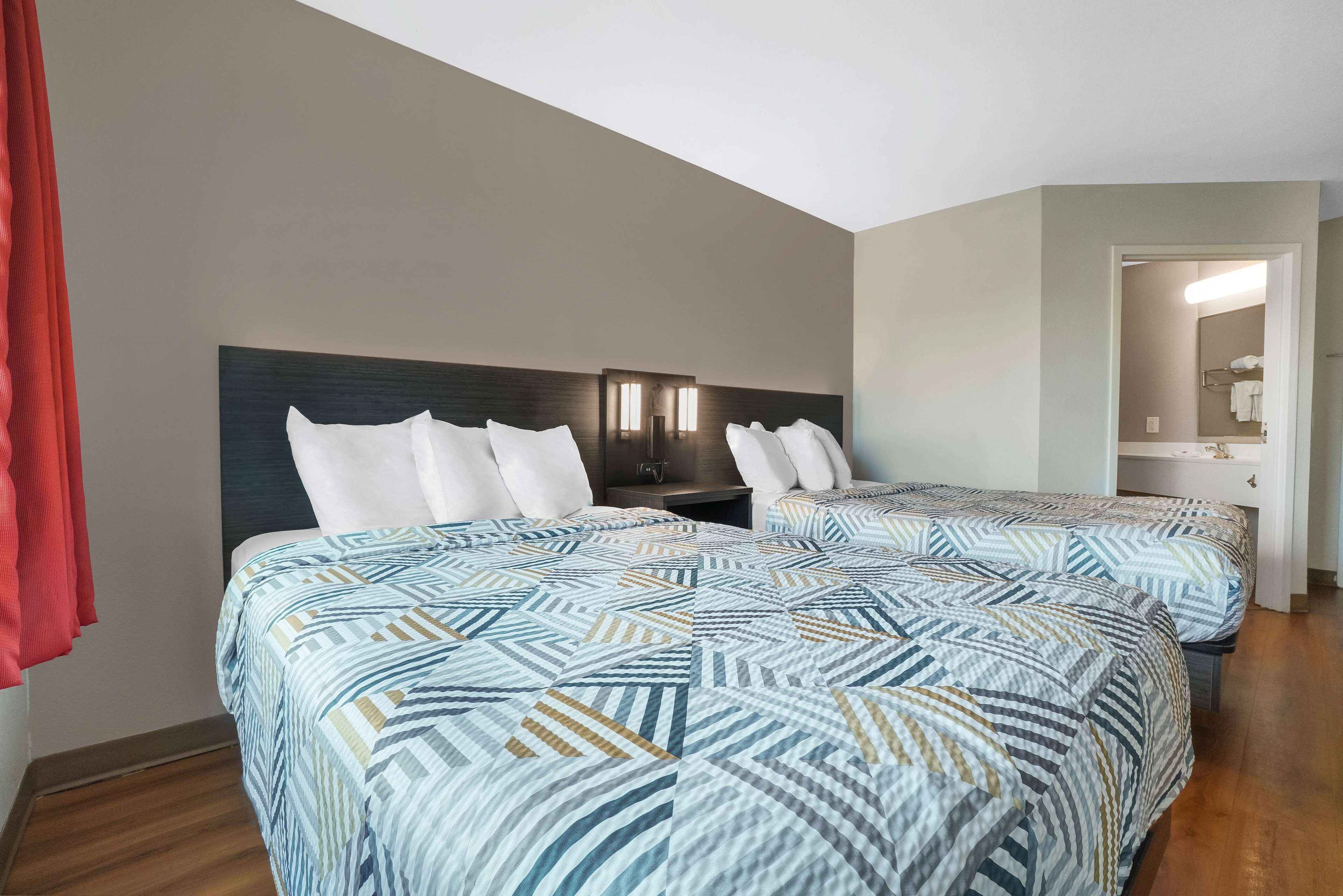 A hotel room with two beds, a nightstand, a mirror, and a door leading to a bathroom.