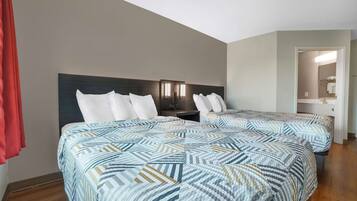 A hotel room with two beds, a nightstand, a mirror, and a door leading to a bathroom.