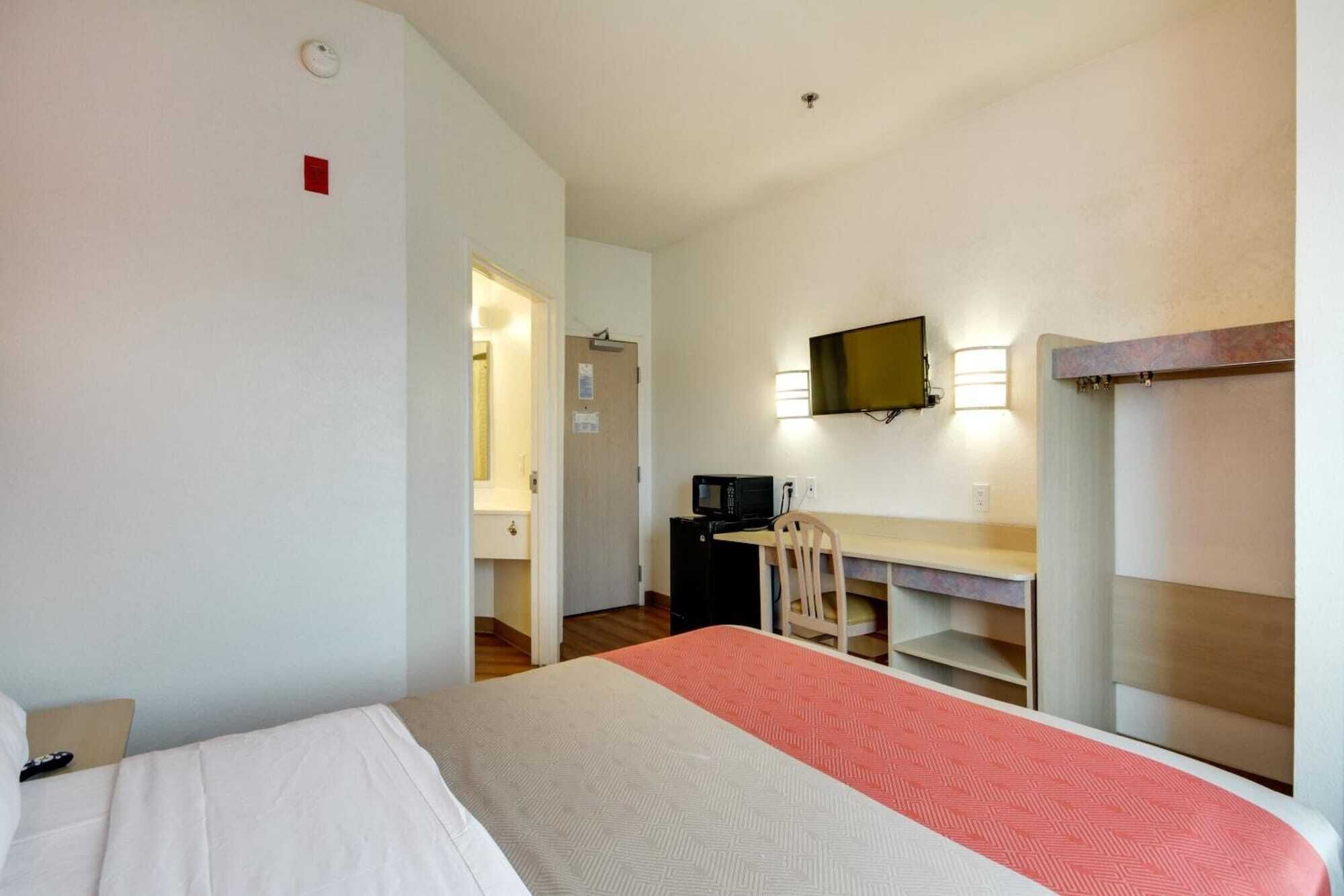 A hotel room with a bed, a desk with a chair, a television, and a microwave.