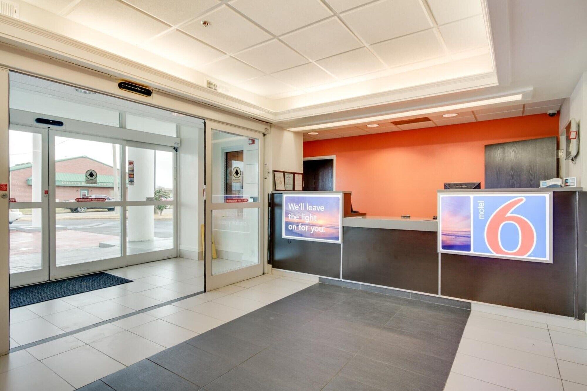 Un hall d’hôtel comprenant un comptoir d’accueil, une entrée avec une porte vitrée et une enseigne indiquant le nom de l’hôtel.